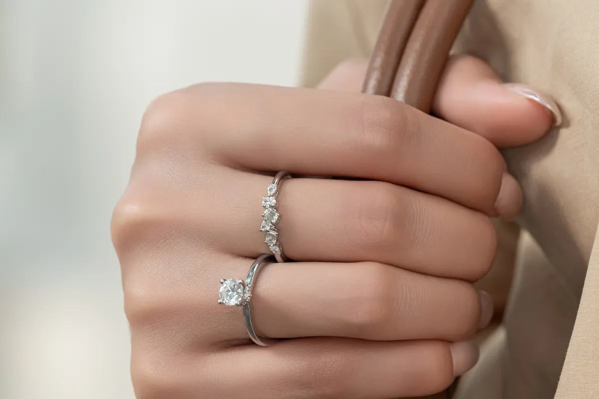 A hand wearing a solitaire and a stacked diamond ring</picture>