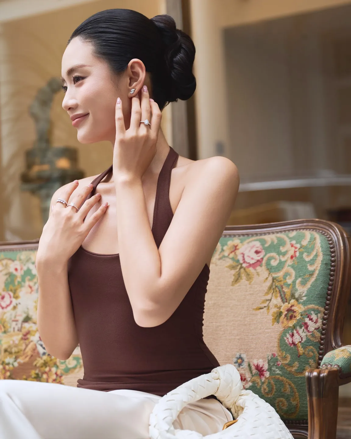 Bàn tay đeo nhẫn kim cương TeeTee&Co., cầm ly rượu vang trắng trên bàn đỏ